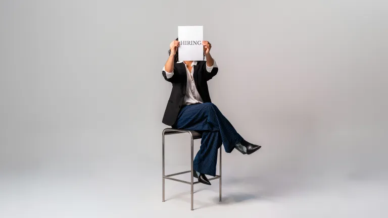 Frau sitzt auf einem Stuhl mit einem Schild, auf dem ‚Wir stellen ein‘ steht