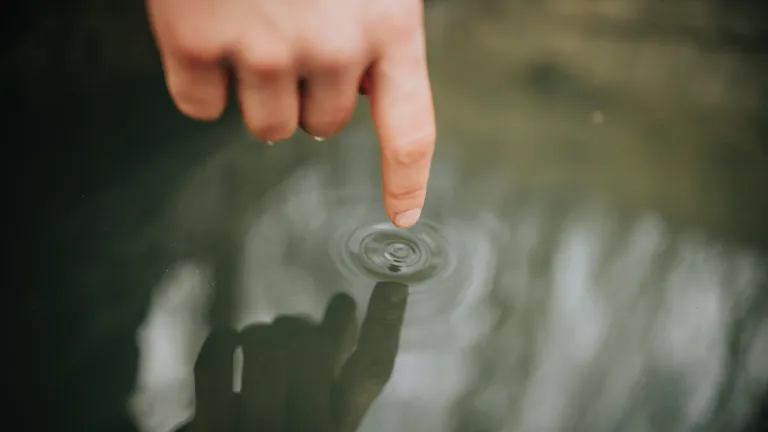 Ein Finger berührt die Wasseroberfläche, Spiegelung der Natur