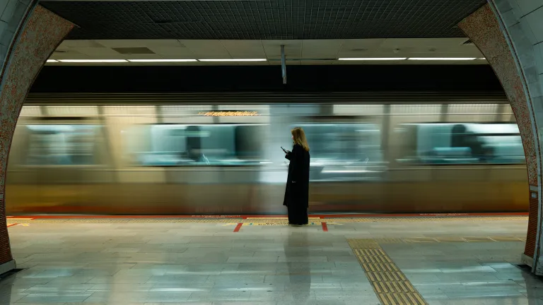 A woman in a tube station looking at her mobile phone as a train passes by