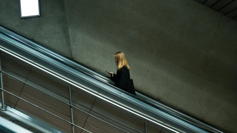 A woman is standing on an escalator looking at her mobile phone