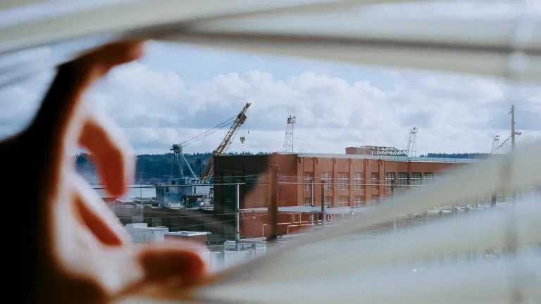 Hand opening window blinds to look out at city
