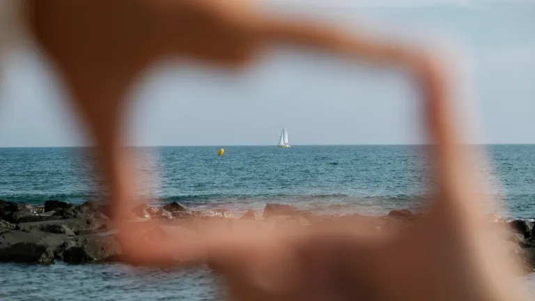 Two hands framing view of boat on sea