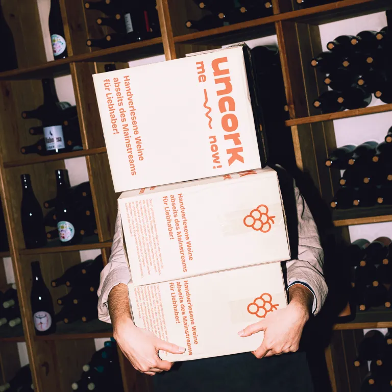 person holding uncork-me-now boxes and wine in the background