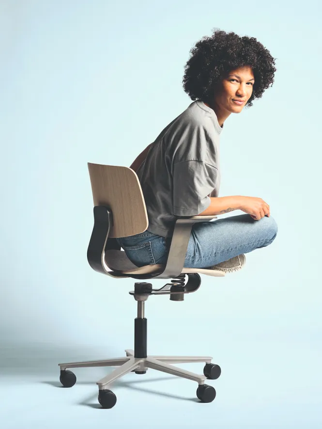 A woman is sitting cross-legged on the WiChair by Wilkhahn