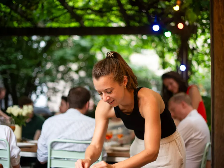 Eine Frau beugt sich über einen Tisch, um Gäste auf einer Outdoor-Party zu bedienen.
