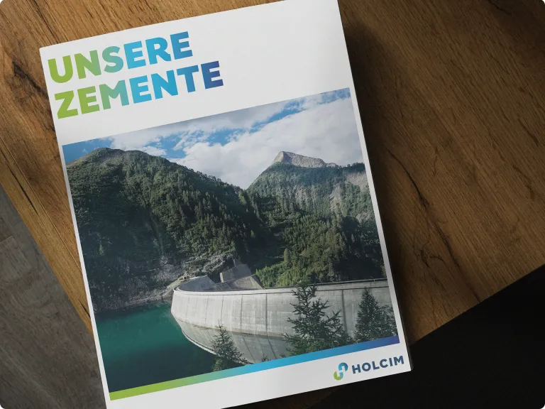 Eine Broschüre mit dem Titel ‚UNSERE ZEMENTE‘ in einer Schrift mit Blau-Grün-Verlauf. Das Cover zeigt ein Foto eines großen Staudamms, eingebettet in ein üppiges, bergiges Tal. Das Holcim-Logo befindet sich unten rechts.