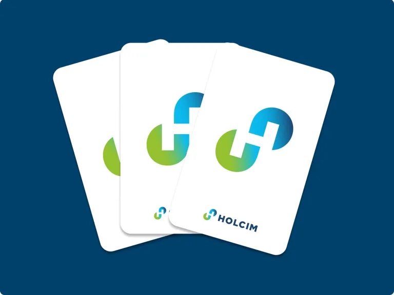 Drei weiße, rechteckige Karten, fächerförmig vor einem dunkelblauen Hintergrund angeordnet. Jede Karte zeigt prominent das Holcim-‚H‘-Unendlichkeitssymbol in einem lebendigen Grün-Blau-Verlauf, mit dem vollständigen Holcim-Logo am unteren Rand.
