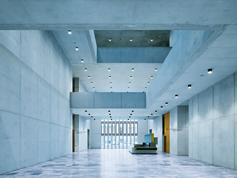 Das minimalistische Atrium der Erweiterung des Kunsthaus Zürich, mit hoch aufragenden grauen Betonwänden und hängenden geometrischen Laufstegen.
