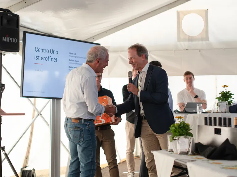 Zwei Personen von Selfrag schütteln sich die Hand vor einer Versammlung von Menschen bei der Einführung von Centro Uno.